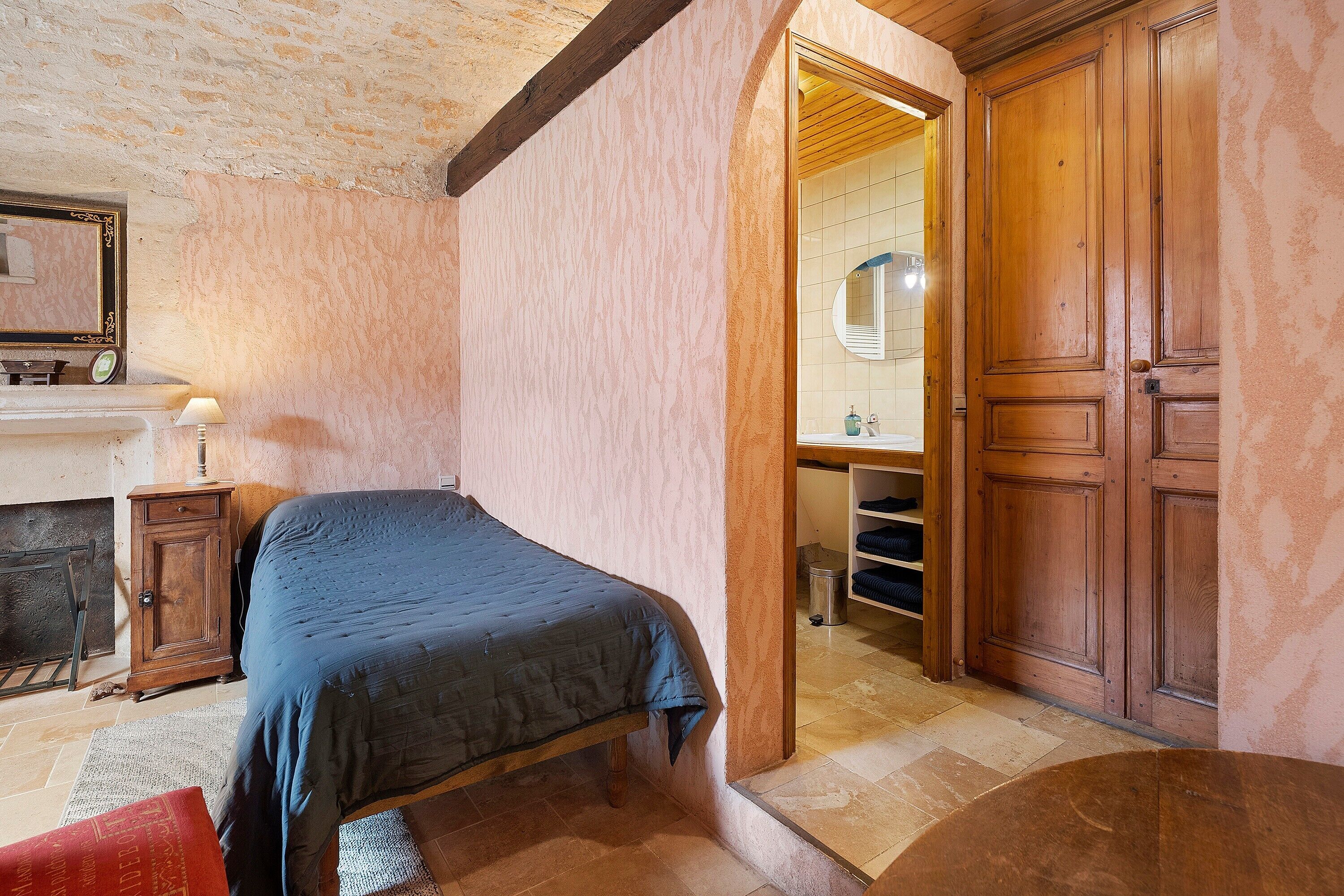 Une chambre à coucher avec un lit, une armoire en bois, un miroir et une petite table avec une lampe.