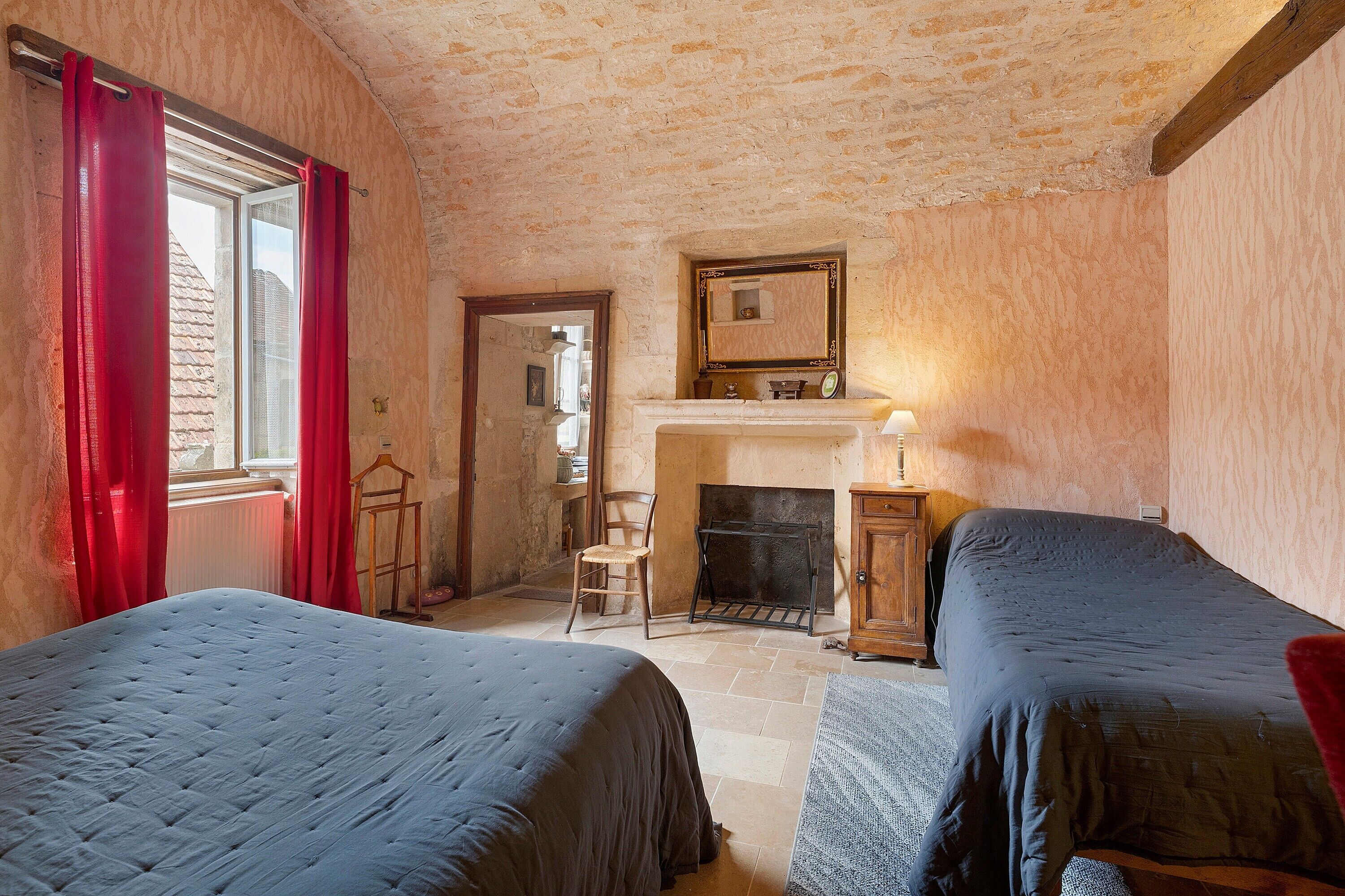 Une chambre avec deux lits, une cheminée et un miroir au mur.