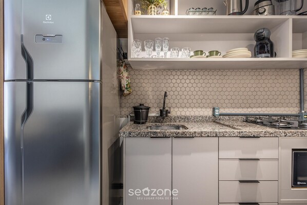A modern kitchen with a stainless steel refrigerator, a granite countertop, and a hexagonal tile backsplash.