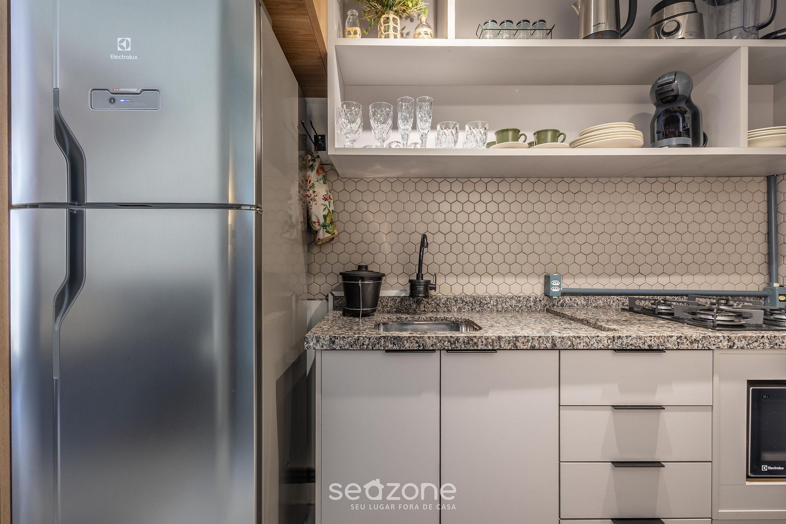 A modern kitchen with a stainless steel refrigerator, a granite countertop, and a hexagonal tile backsplash.