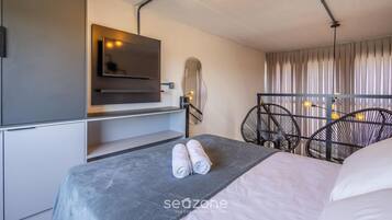 Una camera d'albergo moderna con un letto, una TV a parete, uno specchio e una lampada a sospensione.
