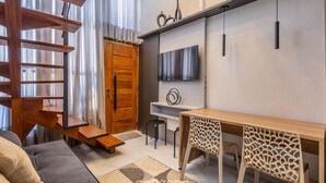 Een moderne woonkamer met een houten trap, een bank, een eettafel en een televisie die aan de muur is bevestigd.