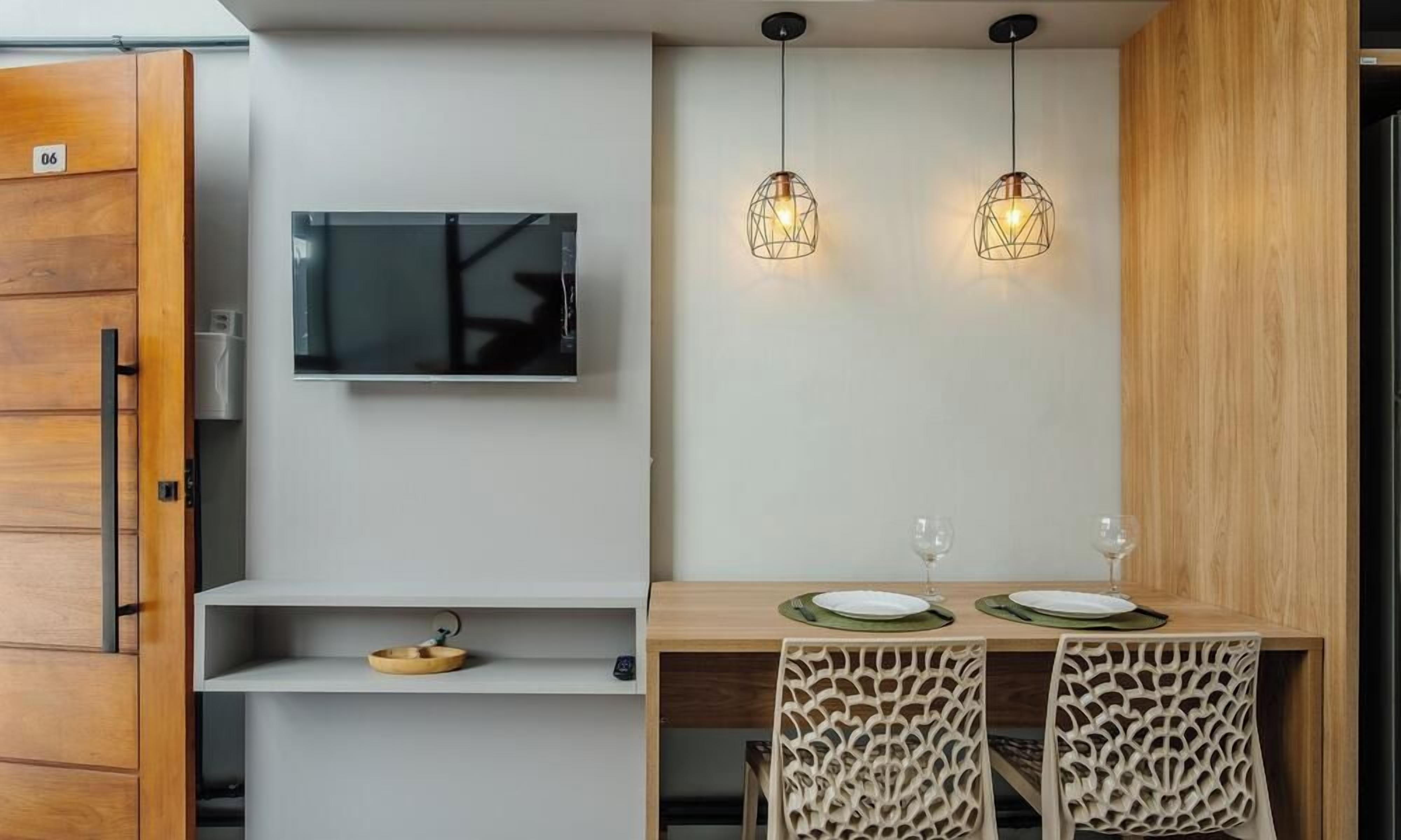 Una cocina moderna con televisor de pantalla plana, luces colgantes y un comedor con una mesa dispuesta para dos.
