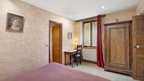 A bedroom with a bed, a desk, a chair, a wardrobe, and a painting on the wall.