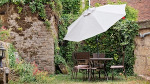 An outdoor seating area with a table and chairs, surrounded by greenery and a stone wall.