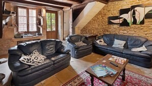 A rustic living room with exposed wooden beams, stone walls, and leather sofas.