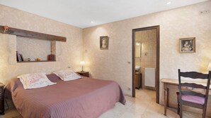 Quarto com cama, mesas de cabeceira, escrivaninha, cadeira, espelho e duas quadros pendurados na parede.