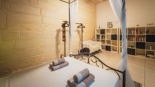 A room with a bed, a bedside table, a bookshelf, and a curtain. - Casa Due Balli | 400-Year Historic Valletta House (Valletta)