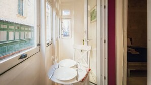 A narrow corridor with a small table set for two, a window, and a door leading to a room with a bed. - Casa Due Balli | 400-Year Historic Valletta House (Valletta)