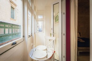 A narrow corridor with a small table set for two, a window, and a door leading to a room with a bed. - Casa Due Balli | 400-Year Historic Valletta House (Valletta)