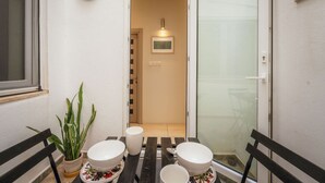 A small outdoor dining area with a table set for two, a potted plant, and a sliding glass door leading to a room. - Casa Due Balli | 400-Year Historic Valletta House (Valletta)