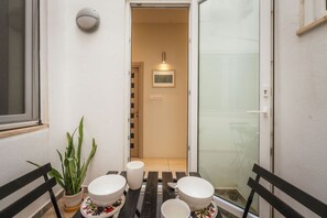 A small outdoor dining area with a table set for two, a potted plant, and a sliding glass door leading to a room. - Casa Due Balli | 400-Year Historic Valletta House (Valletta)