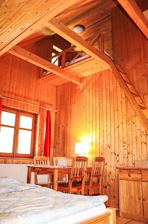A wooden cabin interior with a bed, a table, chairs, and a window.
