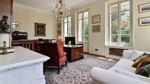 A spacious room with a marble fireplace, a red leather chair, a white sofa, and a large window with a view of trees. - Classic South of France elegances set in an oasis in the heart of Cannes (Cannes)