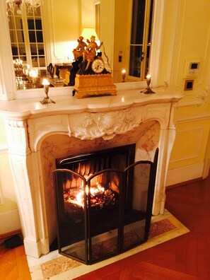 A fireplace with a fire, a mantel with decorative items, and a mirror above it. - Classic South of France elegances set in an oasis in the heart of Cannes (Cannes)