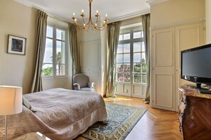 A hotel room with a large bed, a television, a chair, and a view of the outside. - Classic South of France elegances set in an oasis in the heart of Cannes (Cannes)