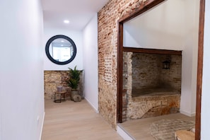 A hallway with a wooden floor, a brick wall, a round mirror, and a stone bench. - NEW Beautifully Restored Historic Apartment (Willemstad)