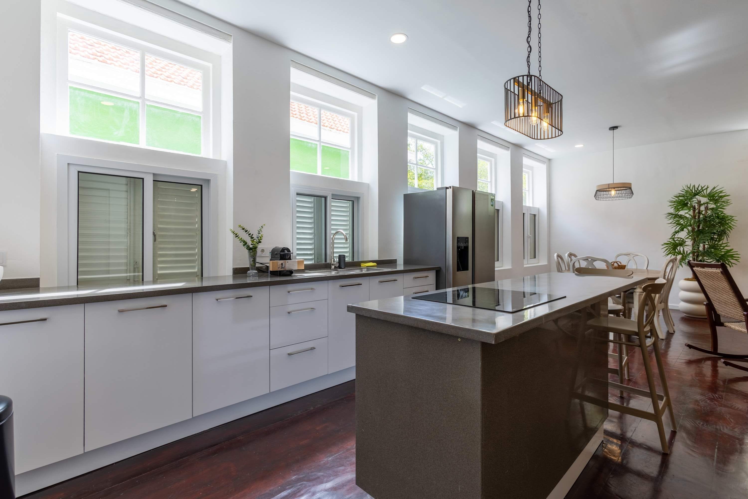 Una cocina moderna con una isla central, ventanas amplias y una zona de comedor con sillas.