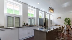 A modern kitchen with a central island, large windows, and a dining area with chairs. - NEW Beautifully Restored Historic Apartment (Willemstad)