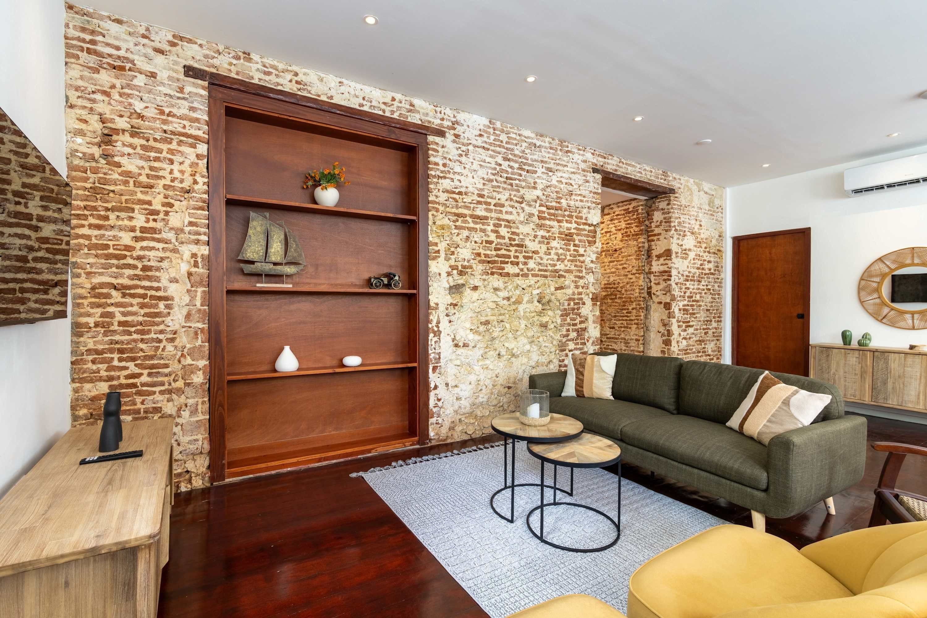A living room with a brick wall, wooden shelves, a sofa, a coffee table, and a small rug.