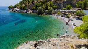 A coastal beach with clear turquoise waters, rocky terrain, and a stone wall along the shore. - Kalymnos Island Gentaway - Chora Central Location (Kalymnos)