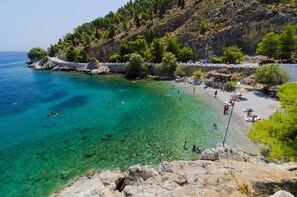 Ein Küstenstrand mit klarem türkisblauem Wasser, felsigem Gelände und einer Steinmauer entlang des Ufers.