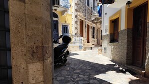 A narrow cobblestone street with a scooter parked on the side, buildings with stone facades, and a clear sky. - Kalymnos Island Gentaway - Chora Central Location (Kalymnos)