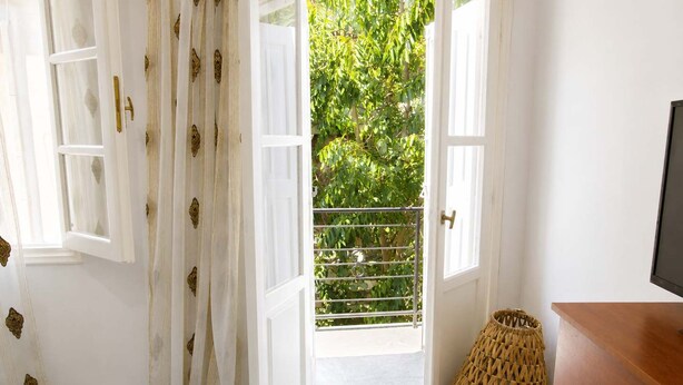 A bedroom with a bed, a wooden dresser, a wicker basket, and a balcony with a metal railing. - Kalymnos Island Gentaway - Chora Central Location (Kalymnos)