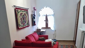 Un salon avec un canapé rouge, une table basse sur laquelle se trouve un plateau de collations, une tasse blanche et une machine à café noire.