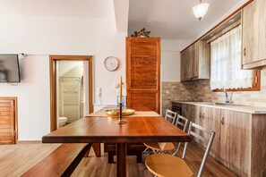 A compact kitchen with wooden cabinets, a dining table with chairs, and a visible clock on the wall. - Stemnitsa Stone Residence - Cosy Mountain Escape (Gortynia)