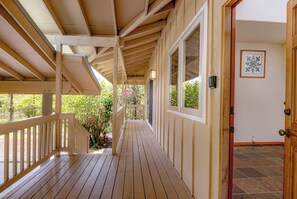 Eine überdachte Holzterrasse mit Geländer, einer Tür rechts und einem Fenster links.