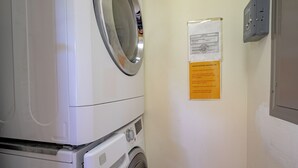 Ein Waschraum mit einer Waschmaschine und einem wandmontierten Trockner. Ein Hinweis an der Wand gibt Anweisungen zur richtigen Nutzung der Waschmaschine.