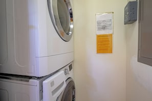 Ein Waschraum mit einer Waschmaschine und einem wandmontierten Trockner. Ein Hinweis an der Wand gibt Anweisungen zur richtigen Nutzung der Waschmaschine.