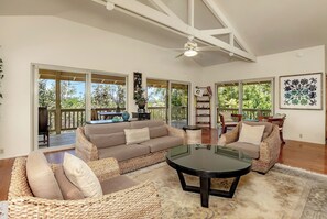 A spacious living area with a sofa, chairs, and a coffee table, featuring large windows and a ceiling fan. - Maluhia Hale - 3BR Private Home Near Hilo (Keaau)