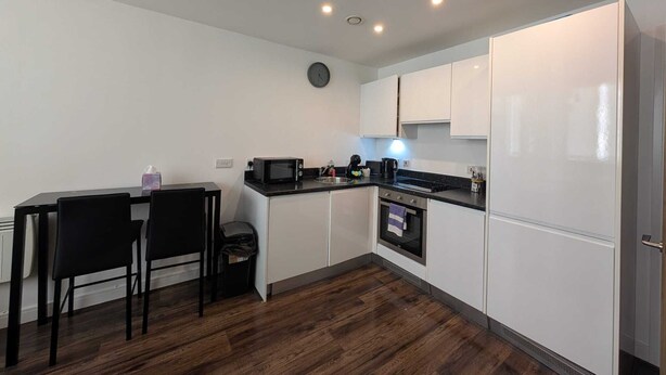 A compact kitchen with white cabinets, a black countertop, a microwave, and a sink. - City View Studio Apartment – Liverpool (Liverpool)