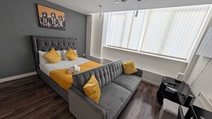 A modern bedroom with a bed, a gray sofa, and a window with blinds. - City View Studio Apartment – Liverpool (Liverpool)