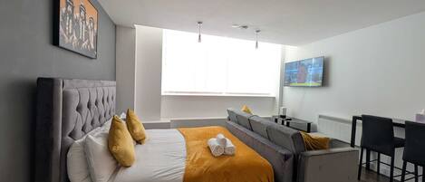A modern bedroom with a large bed, a desk, and a television.