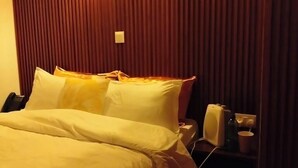 Una habitación de hotel con cama, mesita de noche y lámpara de pared.