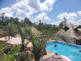 Una piscina con una persona nadando, rodeada de palmeras y construcciones de techo de paja.
