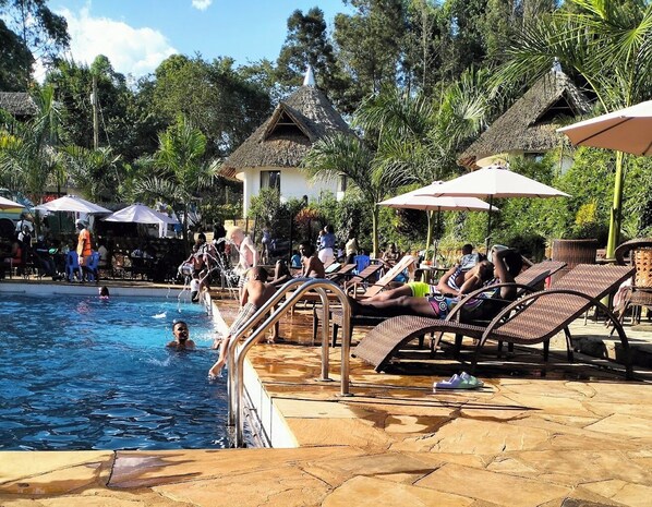 A swimming pool area with lounge chairs and umbrellas, surrounded by trees and buildings.
