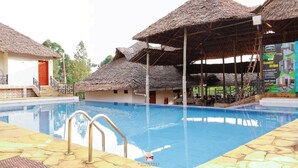 Una piscina con una estructura de techo de paja y un suelo de baldosas de piedra.