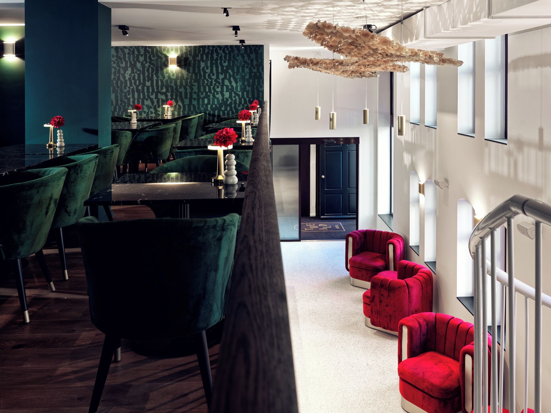 Um hall de hotel moderno com poltronas de veludo verde, sofás vermelhos e uma luminária pendente única.