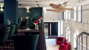 Um hall de hotel moderno com poltronas de veludo verde, sofás vermelhos e uma luminária pendente única.