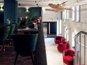 A modern hotel lobby with green velvet chairs, red sofas, and a unique hanging light fixture. - The ALD Boutique Apartments (Den Haag)