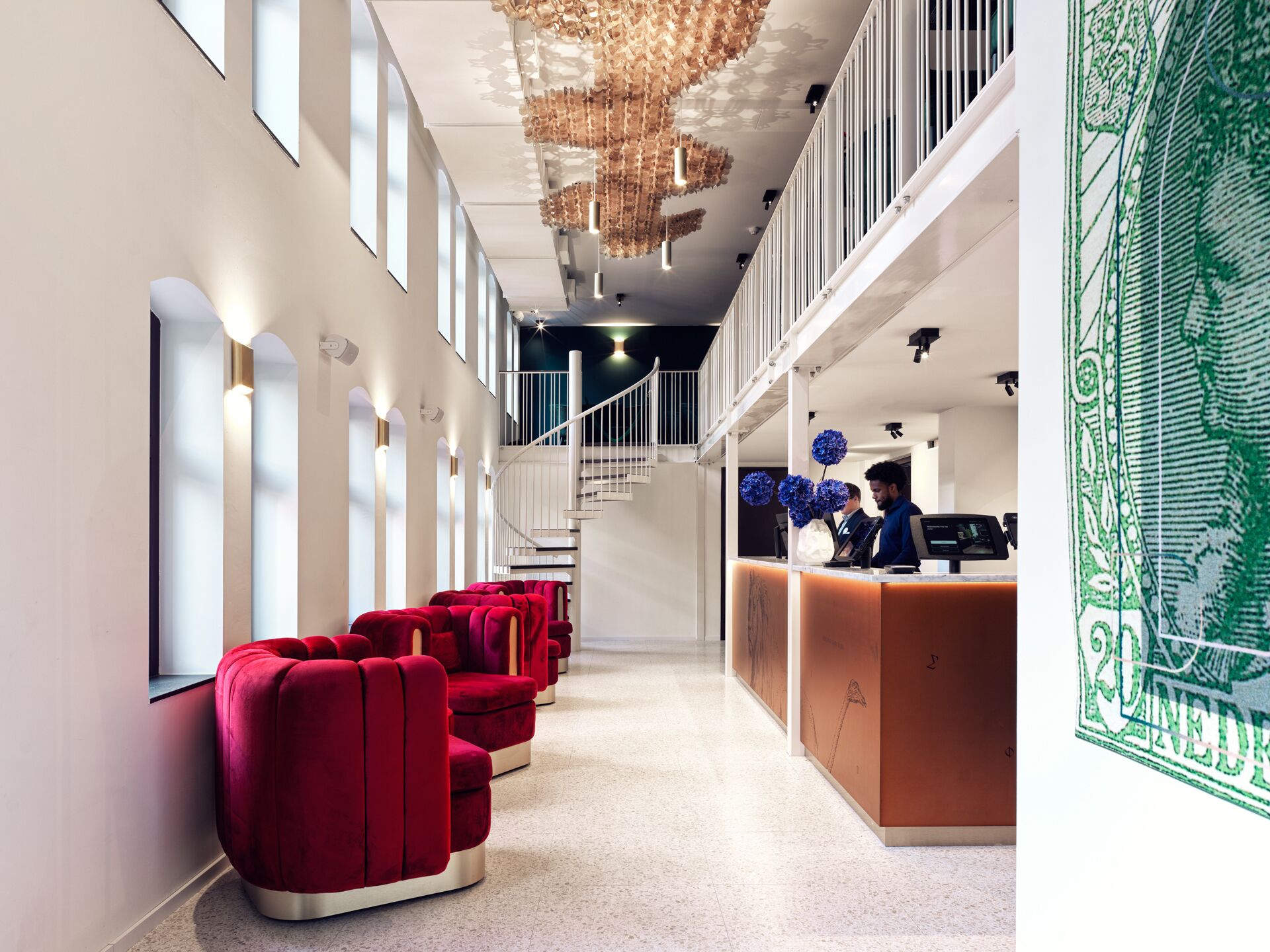 A hotel lobby with a reception desk, red seating, a staircase, and a decorative ceiling.
