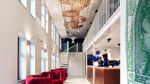 A hotel lobby with a reception desk, red seating, a staircase, and a decorative ceiling.