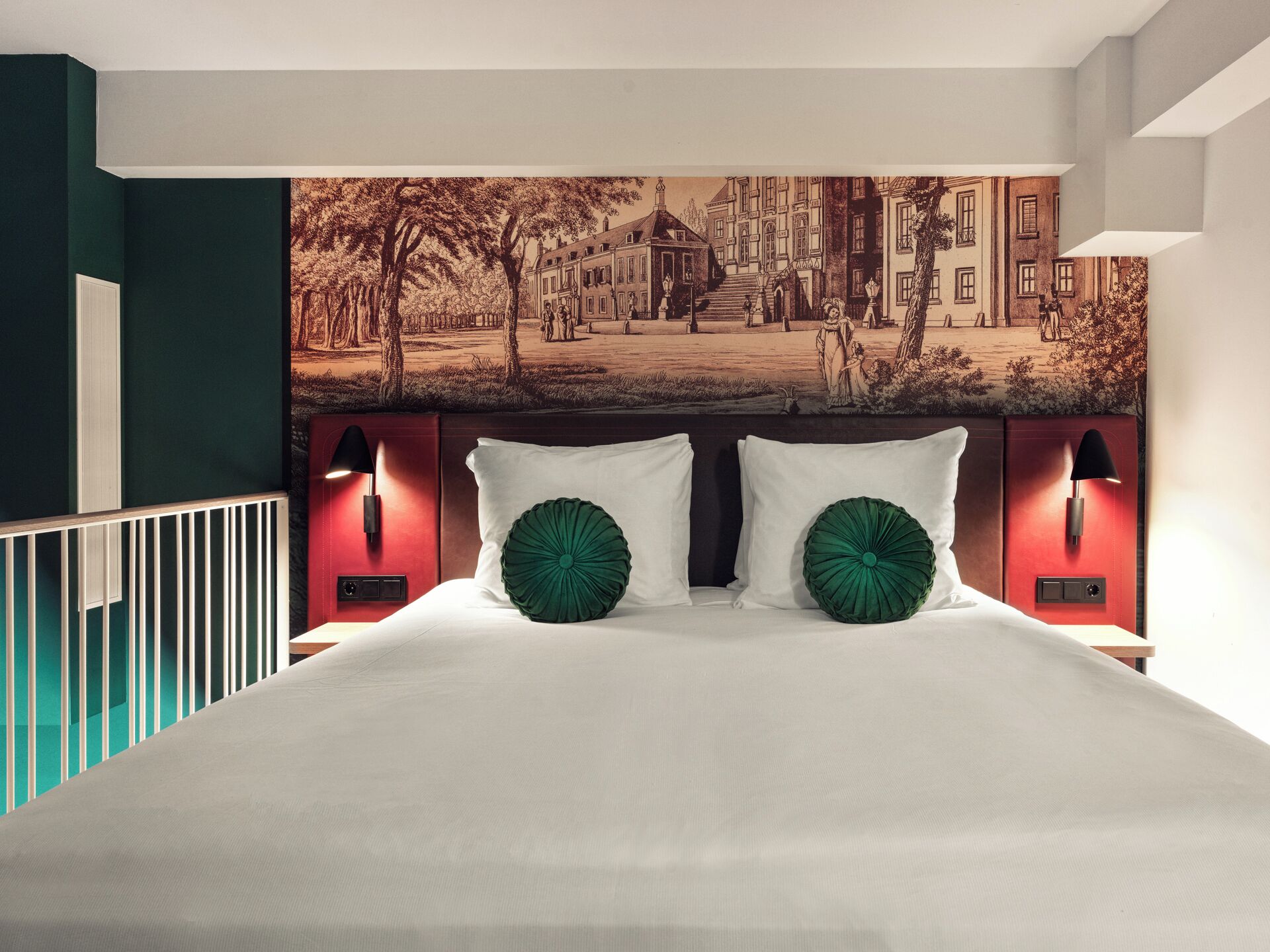 Quarto com uma cama grande, duas almofadas decorativas verdes, cabeceira com luzes fixadas na parede e um mural com vista para a cidade acima da cama.