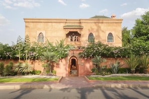 A building with a central entrance, flanked by two symmetrical wings, surrounded by a garden with various plants and flowers. - Villa Taj Sofia & Spa (Marrakech)