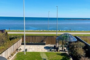 Un espace patio agrémenté d’un belvédère en verre, offrant une vue sur la mer et délimité par une clôture en bois.