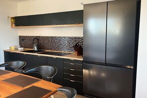 Une cuisine moderne dotée d’un réfrigérateur en acier inoxydable, de meubles de couleur noire, d’un pare-feu en carreaux et d’une table à manger en bois avec des chaises.